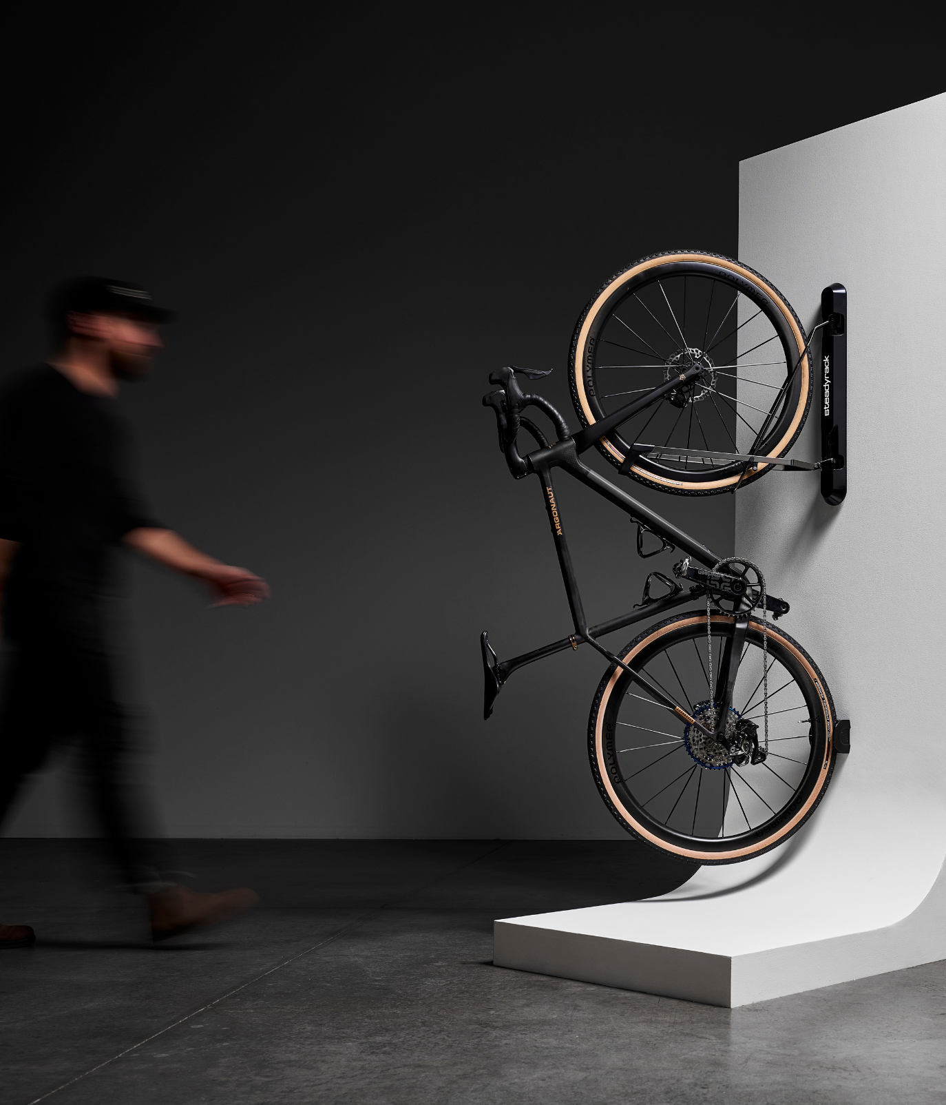 A blurred person walking towards a bike stored in a ProFlex Rack on a white wall.