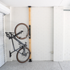 Bicycle stored vertically on a wall-mounted rack on a wooden pole in a garage.