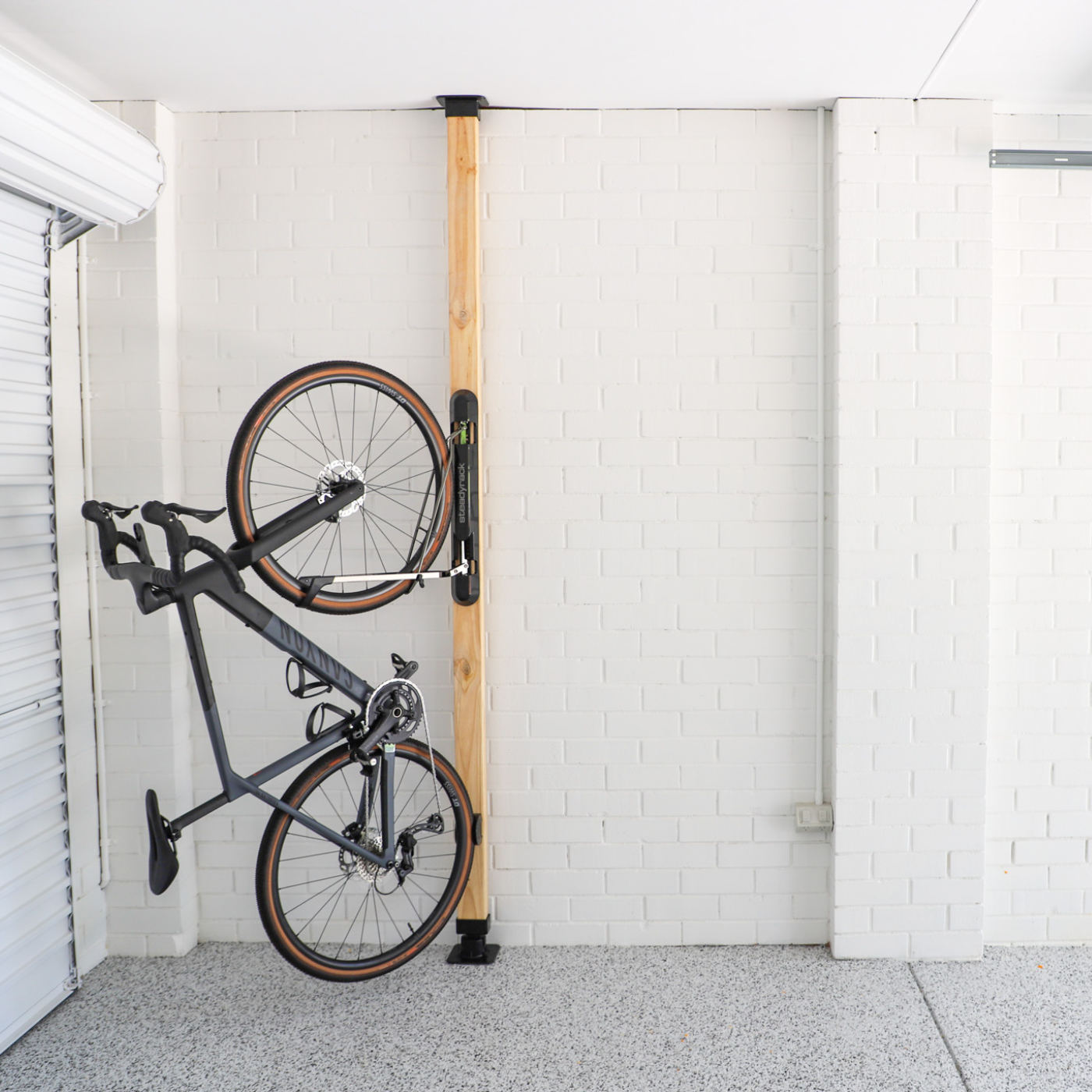 Bicycle stored vertically on a wall-mounted rack on a wooden pole in a garage.