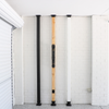 Three wooden poles with black bases leaning against a white brick wall.