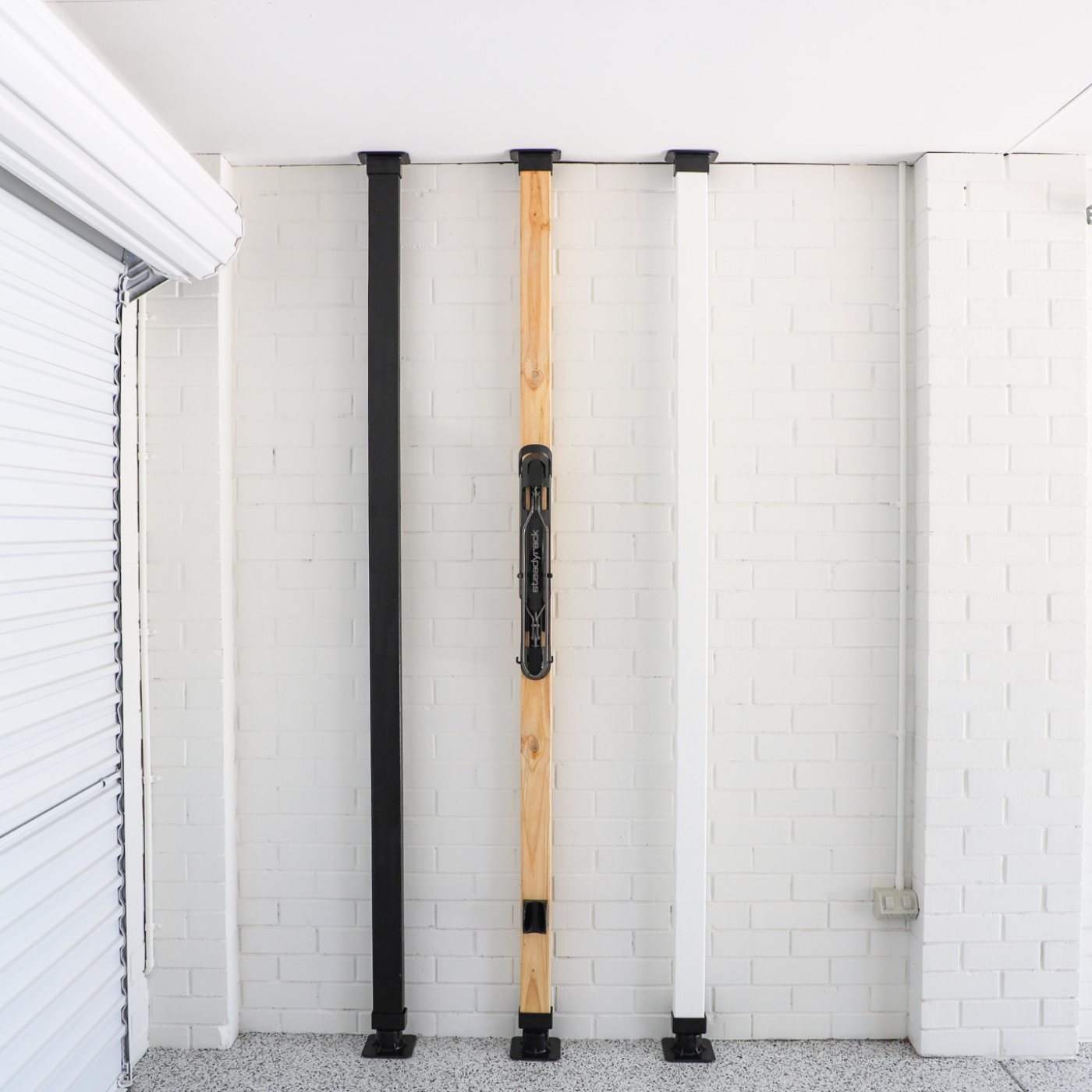 Three wooden poles with black bases leaning against a white brick wall.
