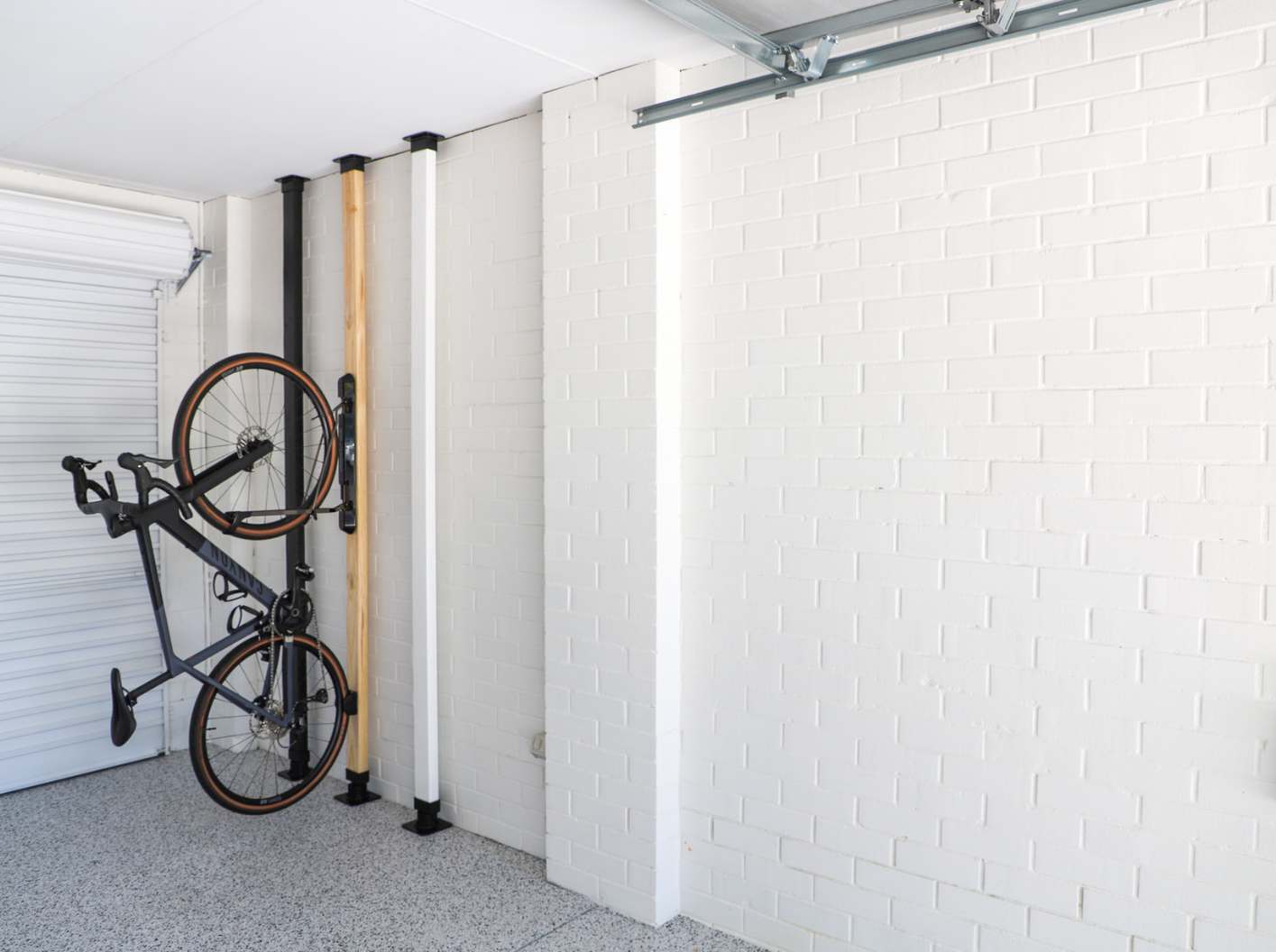 Bicycle mounted on a wall rack in a garage with white bricked walls.