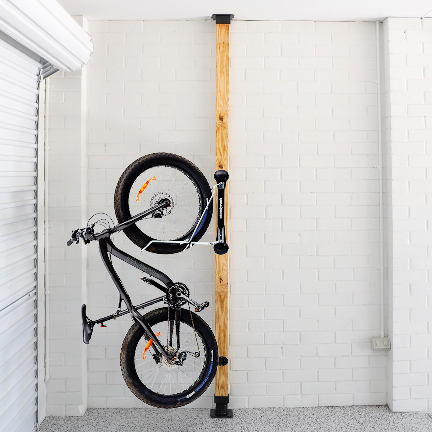 Bicycle mounted against a wooden post with white brick walls.